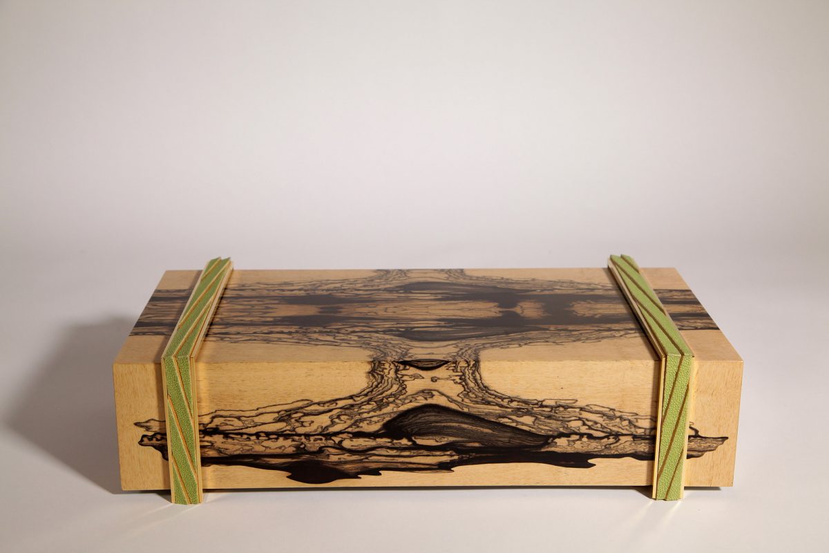 Coffret en bois clair orné de veines sombres, création artisanale illustrant un meuble à secrets sur-mesure avec mécanismes invisibles et finitions contemporaines.